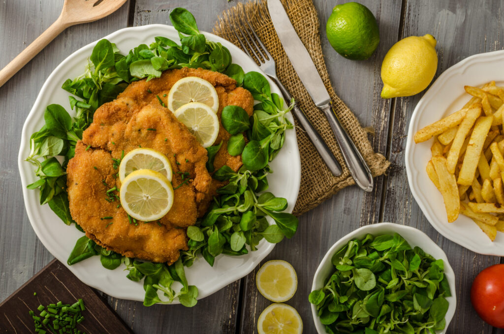 German schnitzel with homemade fries, lemons and limes, tomatoes and lamb's lettuce salad