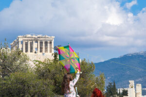 A young girl holding onto a kite as it flies in a deep blue sky . Acropolis , Athens, Greece