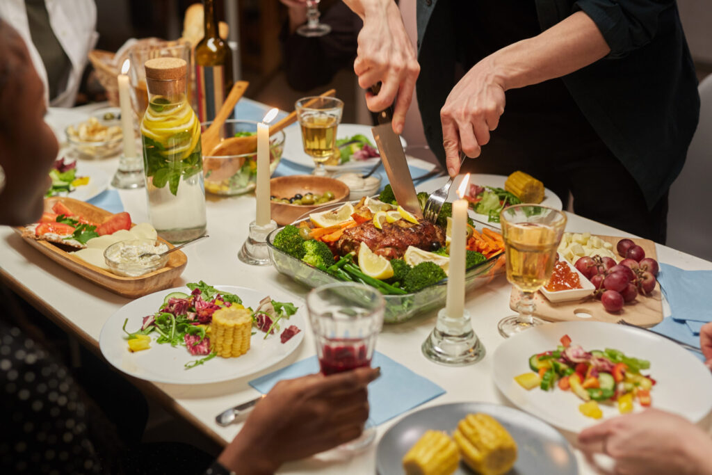 Close-up of people sitting at the holiday table and eating roast beef with vegetables and drinking wine