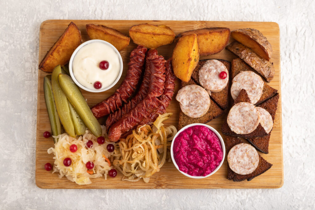 set of snacks: sausages, toast, sauerkraut, marinated onion and cucumber, baked potato on a cutting board on a gray concrete background. Top view, flat lay, close up.