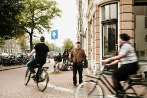 People cycling through a residential Amsterdam street with classic buildings—daily life scene reflecting urban lifestyle and Amsterdam living cost.