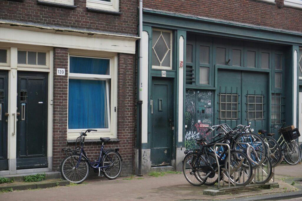 A row of bicycles chained to a compact bike rack outside a traditional Dutch townhouse, surrounded by graffiti—highlighting a common “bad things about living in Netherlands” complaint: overcrowded bike parking and risk of vandalism.