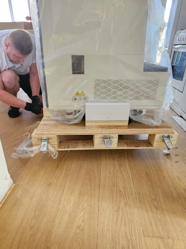 A mover fastens protective wooden planks around a heavy appliance inside a home, illustrating meticulous preparation for international transport.