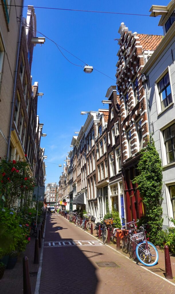 Sunlit Amsterdam canal street lined with narrow gabled houses and parked bikes, showcasing affordable everyday life in the Netherlands.