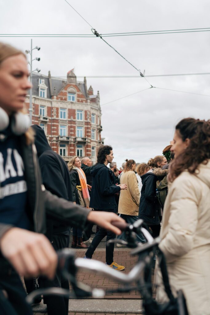 Commuters cycling past historic brick buildings under tram wires, illustrating cost-effective Dutch transport compared to the UK.