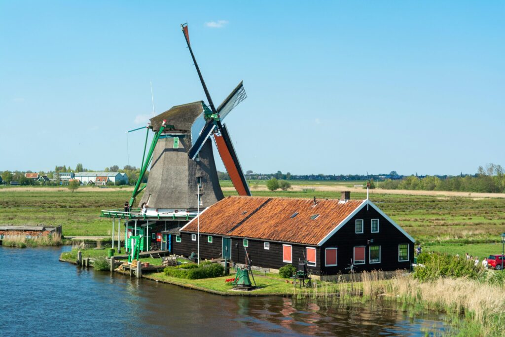 Traditional Dutch windmill and farmhouse in lush green polders under a clear blue sky, reflecting rural life in the Netherlands countryside.