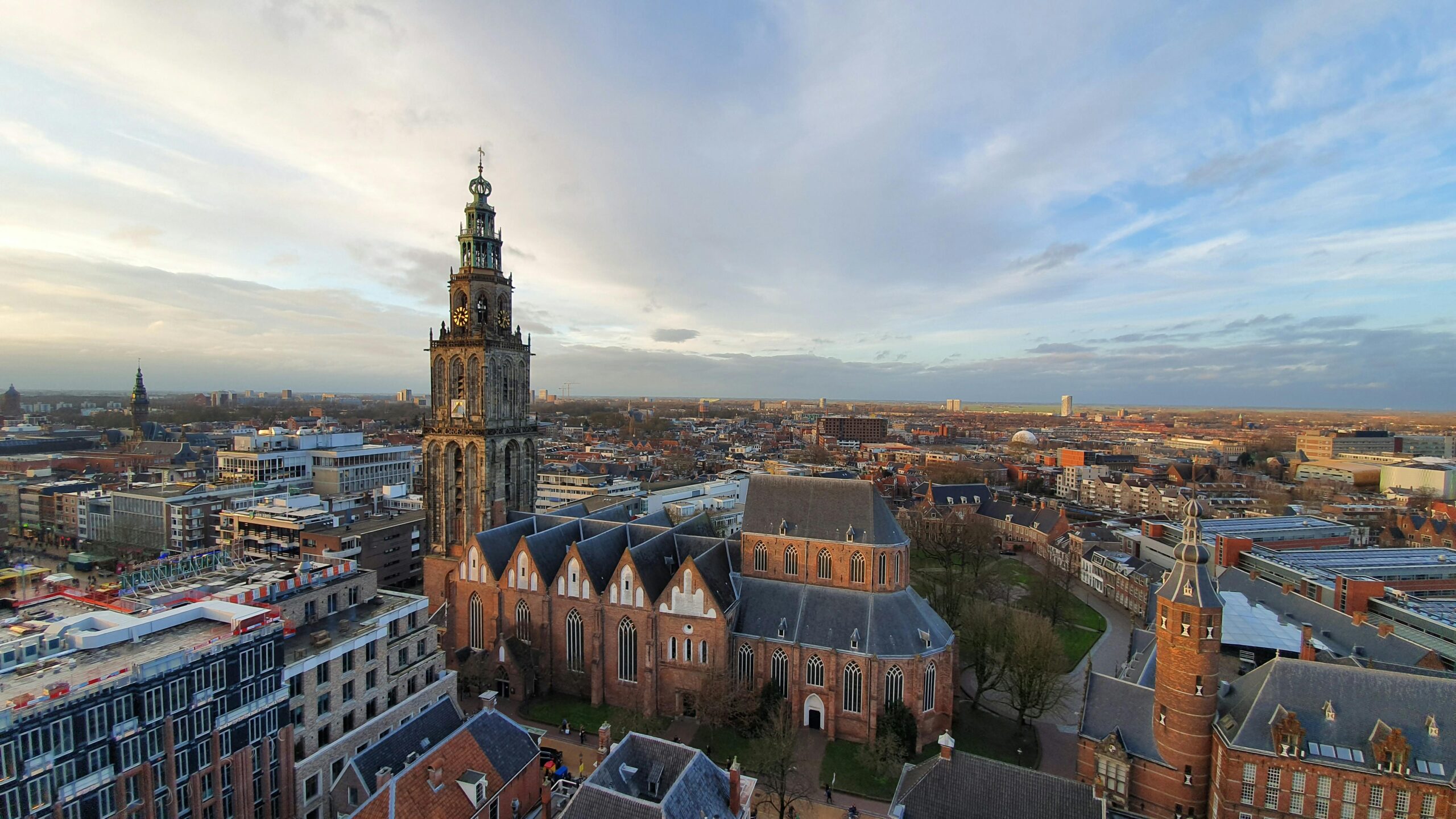 Aerial view of a Dutch city featuring a Gothic church tower and red-roofed buildings, showcasing cityscapes in life in the Netherlands.