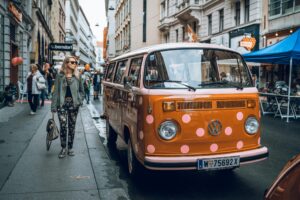 Street scene in Austria featuring a vintage Volkswagen van with pink polka dots, stylish pedestrians, and ornate buildings, capturing the cultural charm and lifestyle nuances in the "living in Austria vs Netherlands" context.