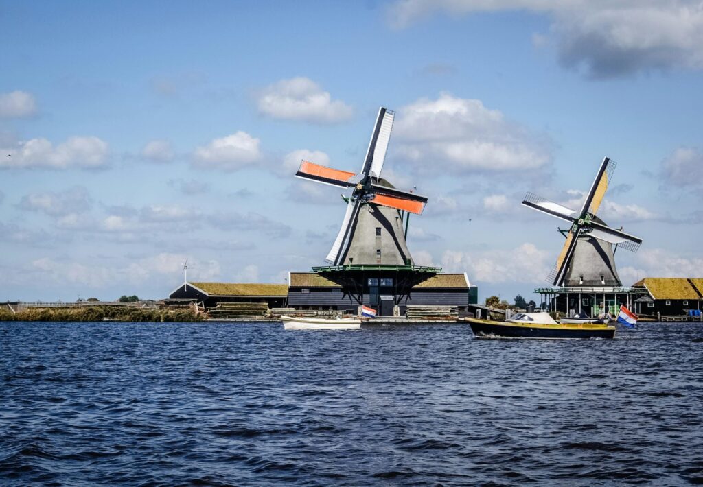 Traditional Dutch windmills on a waterside farm under blue skies—illustrating living in ireland vs netherlands and the iconic Netherlands landscape.