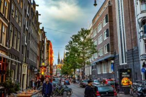 Busy street in central Amsterdam with bikes, cafés, and pedestrians—urban lifestyle scene illustrating living in Netherlands vs Germany comparison.