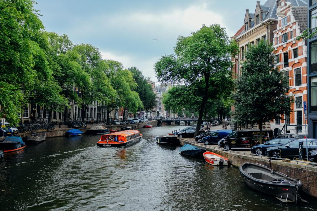 Tour boat cruising through Amsterdam’s scenic canal lined with Dutch townhouses, showcasing the picturesque urban experience of living in Poland vs Netherlands.