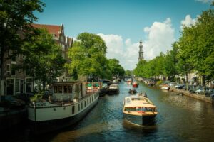 Scenic Dutch canal in Amsterdam with boats and classic architecture, illustrating the structured, water-centric lifestyle of living in the Netherlands.
