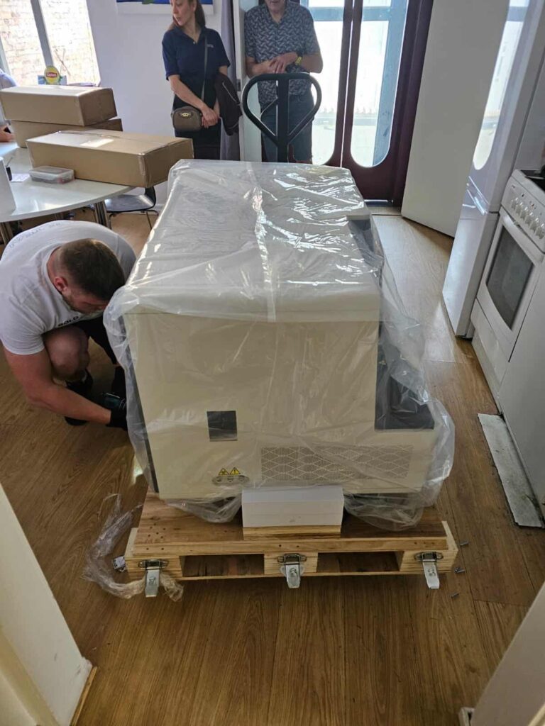 Refrigerator wrapped in protective plastic on a wooden pallet inside a home, set for moving from UK to Amsterdam.