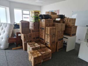 Room filled with stacked moving boxes, furniture, and packed items, all organized for moving from UK to Amsterdam.