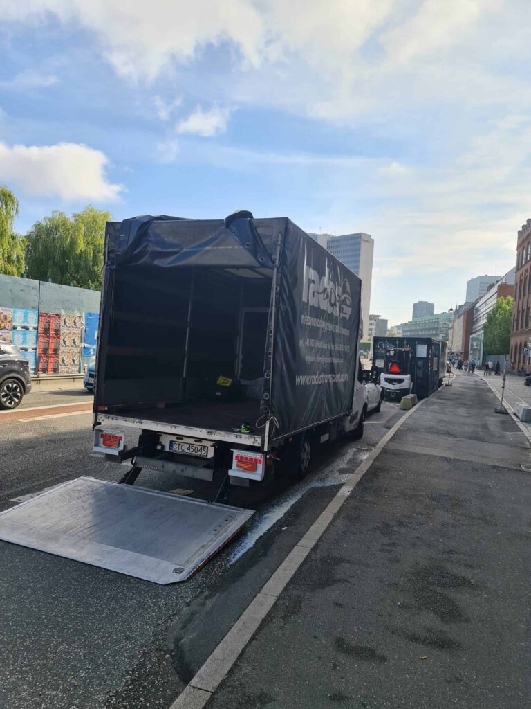 Van with open cargo area and lowered liftgate parked on a city street, ready for moving from UK to Amsterdam.
