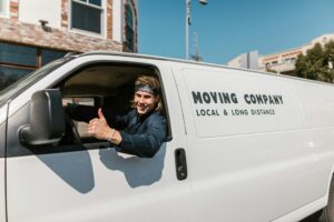 Mover giving thumbs up from the driver’s seat of a van marked ‘Moving Company Local & Long Distance,’ ready for moving to Holland from UK.