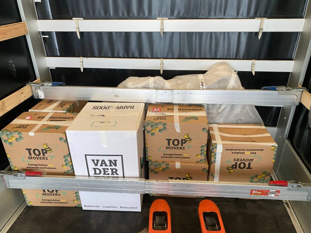 Interior of a moving van with neatly stacked cardboard boxes labeled “Top Movers” and “Vander,” illustrating professional packing for pros and cons of moving to Netherlands.