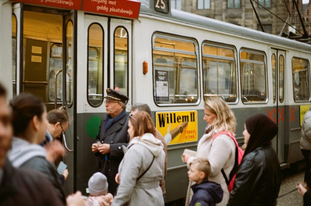 Passengers boarding a classic Dutch tram in a tree-lined street, highlighting everyday public transport options when relocating to the Netherlands.