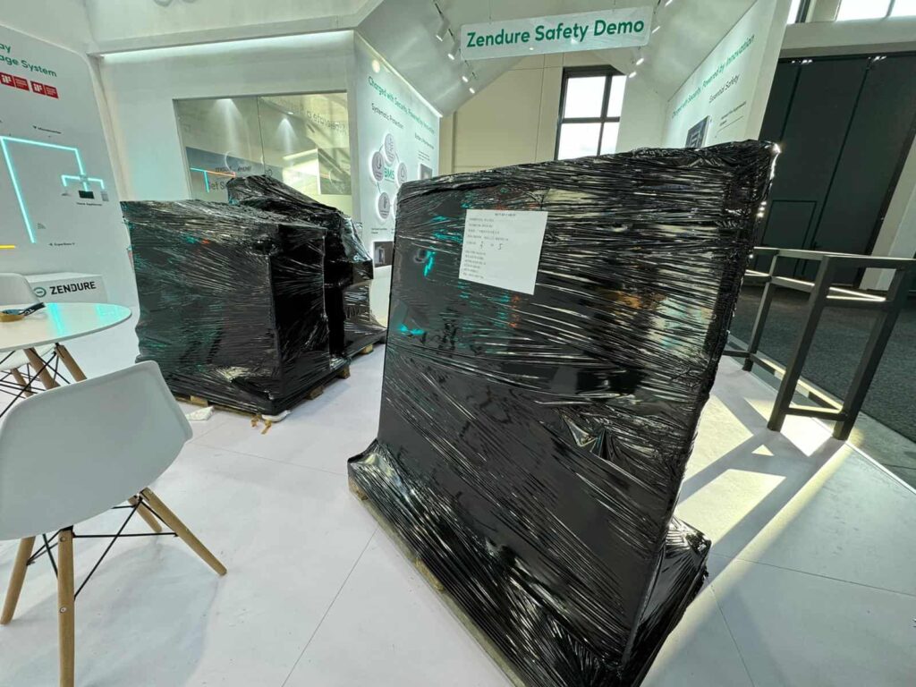Large furniture pieces tightly wrapped in black plastic on wooden pallets, staged indoors for relocation to Netherlands.