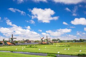 Windmills and green polders beneath a blue sky, symbolizing work–life balance and quality of life tied to a competitive Netherlands salary.