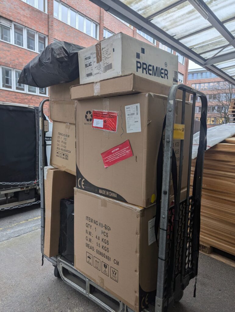 Stacked cardboard boxes on a wheeled pallet jack outside a building, prepared for small removals to Netherlands delivery.