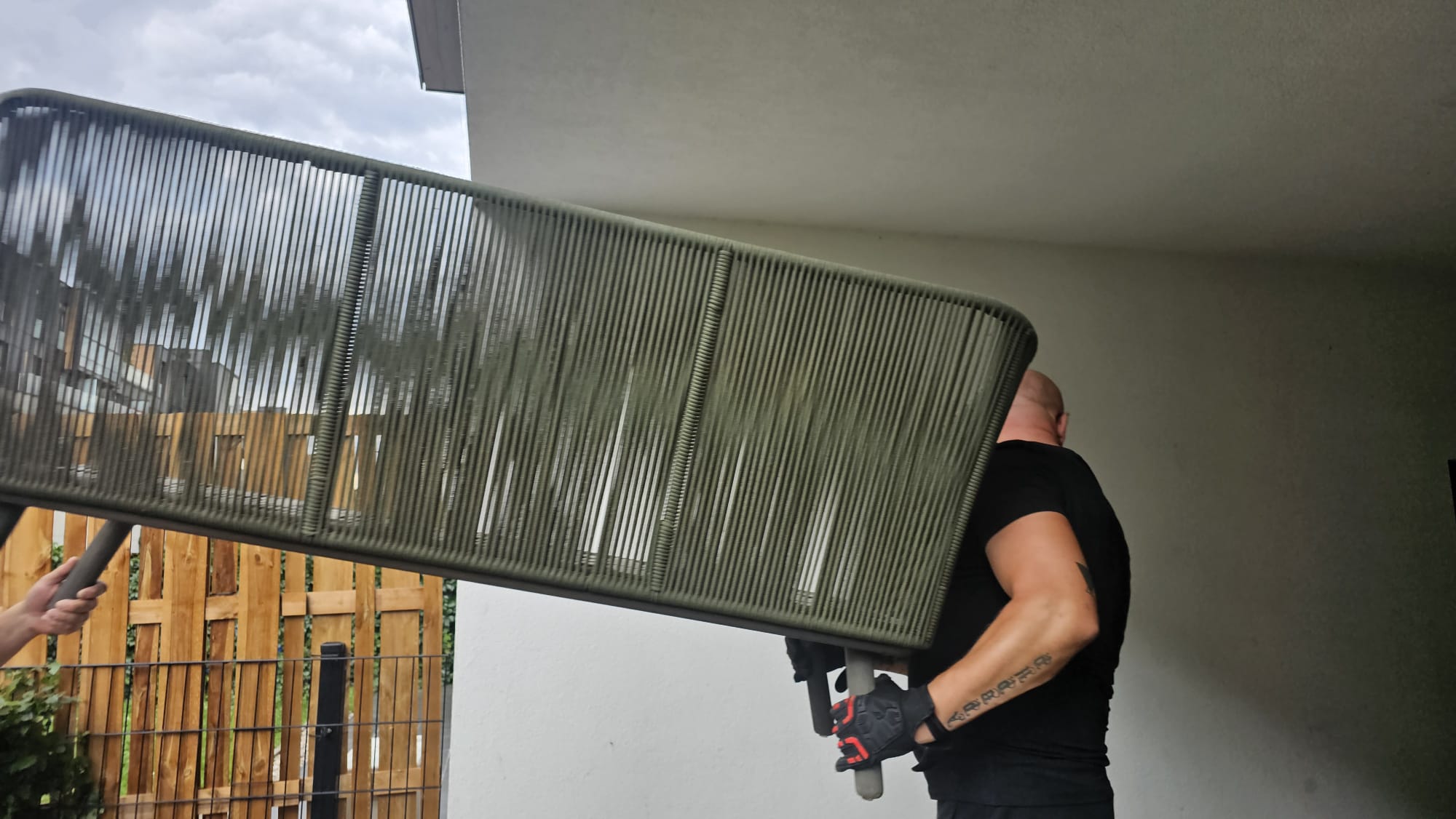 Mover carrying a large outdoor bench on his shoulder while moving furniture from a balcony.