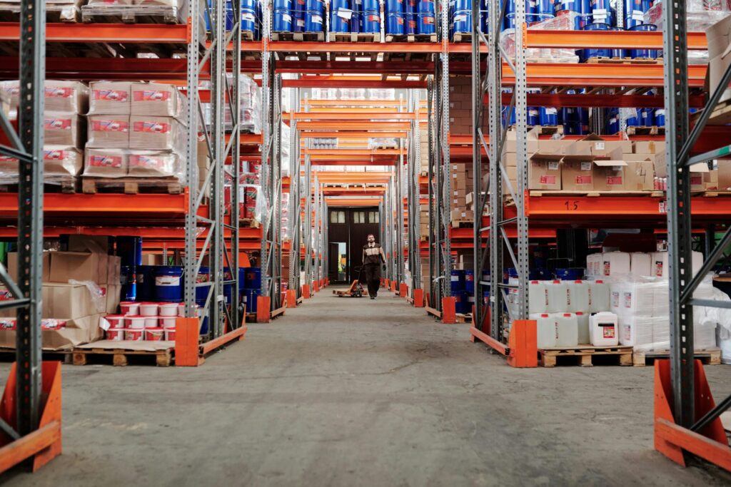 Warehouse aisle with tall shelves full of pallets and cartons, representing VANonsite warehouse storage for European removals and international logistics.