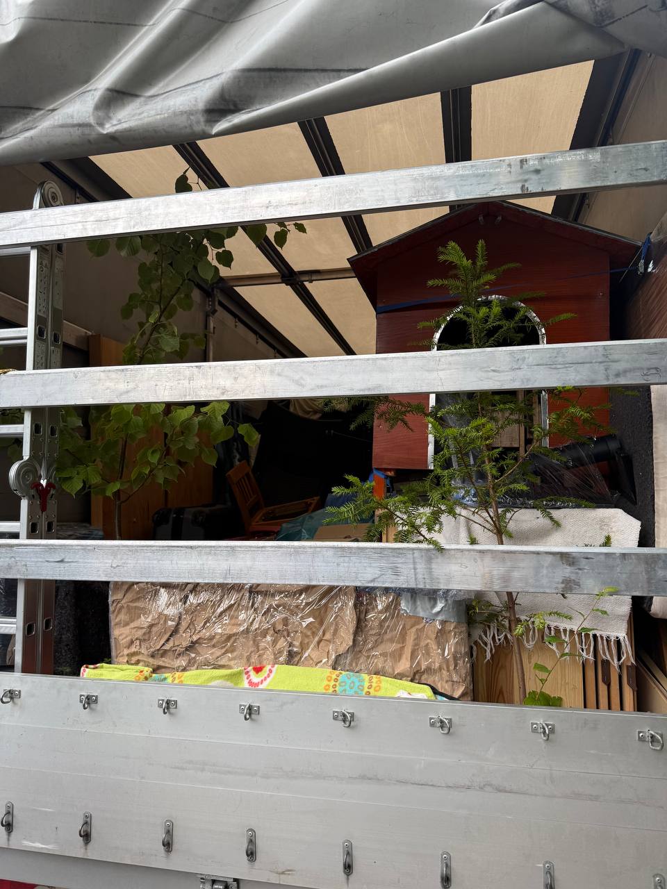Open sided removal truck loaded with plants, furniture and household items, ready for relocation from Germany to Italy.