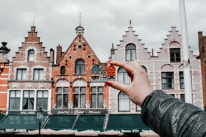 Hand holding a colorful Bruges house souvenir in front of traditional Flemish buildings in Bruges, Belgium
