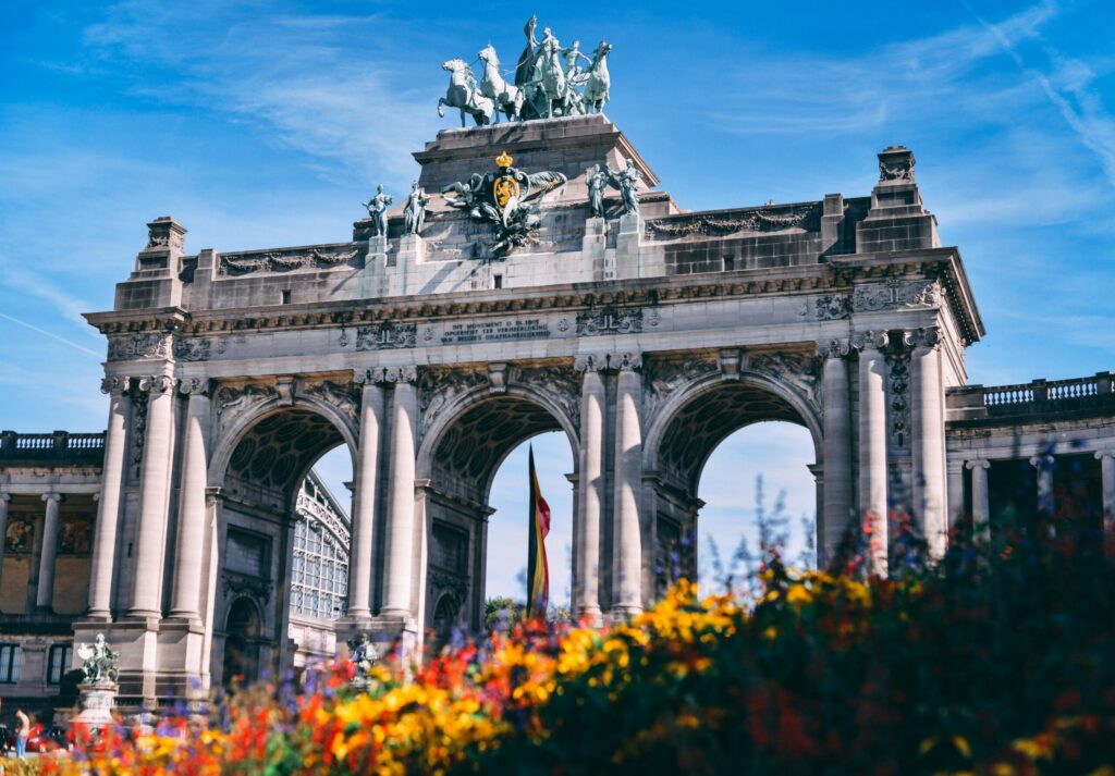 Cinquantenaire Arch in Brussels on a bright day with colorful flowers in the foreground, representing life in Belgium after moving with VANonsite European removals