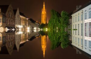 Night view of Bruges canal with illuminated Church of Our Lady and historic Belgian houses reflected in the water, showing the charm of moving to Belgium with VANonsite European removals