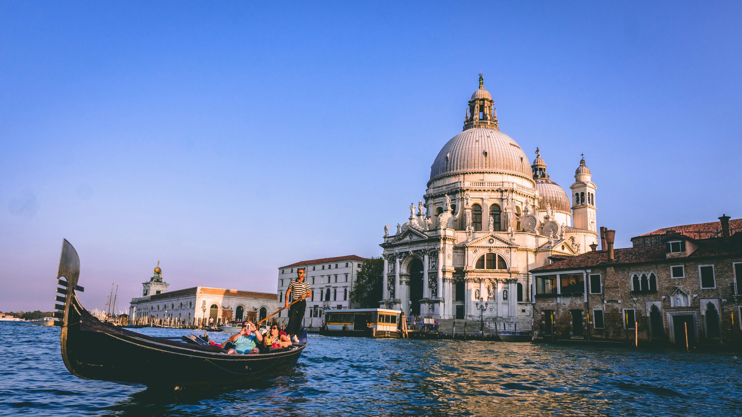 Gondola on a sunny Venice canal passing the Basilica di Santa Maria della Salute, symbolising a relaxed lifestyle after moving to Italy with VANonsite European removals