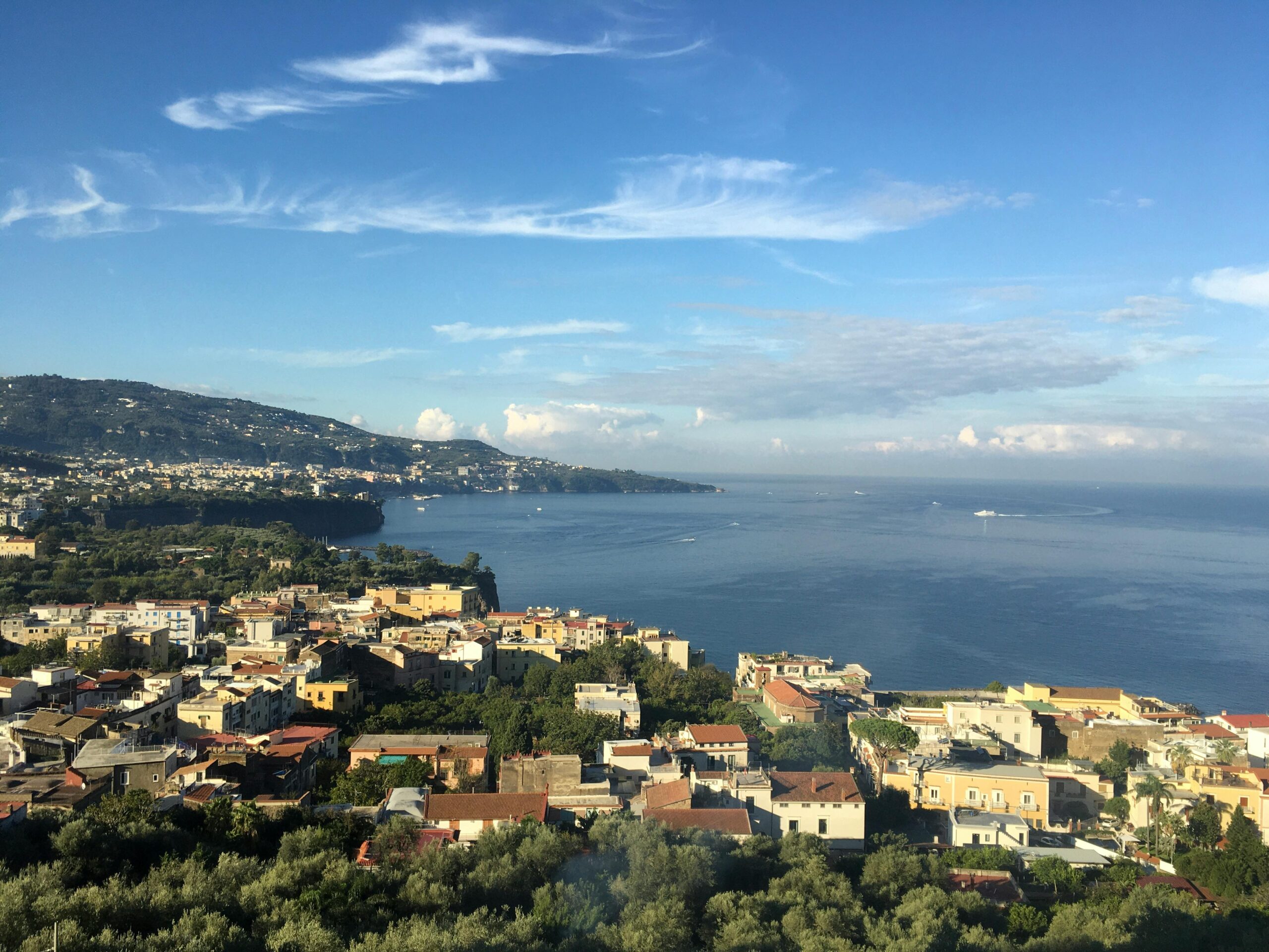 Italian coastal town with colorful houses and boats on a calm blue bay, representing life after moving to Italy with VANonsite European removals